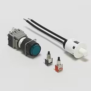 A collection of electronic switches and push button components is displayed on a neutral background. The set includes a large push button with attached wires, a rotary switch, and two small tactile switches with colored bases.