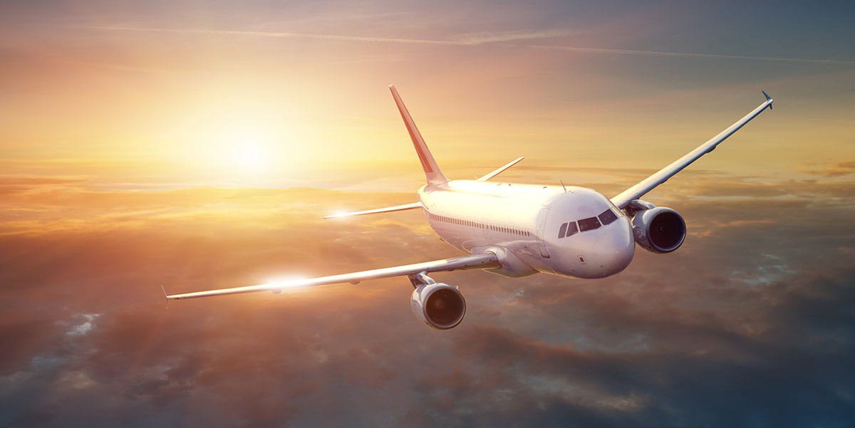 A modern commercial airplane is captured mid-flight above a blanket of clouds during a vibrant sunset.