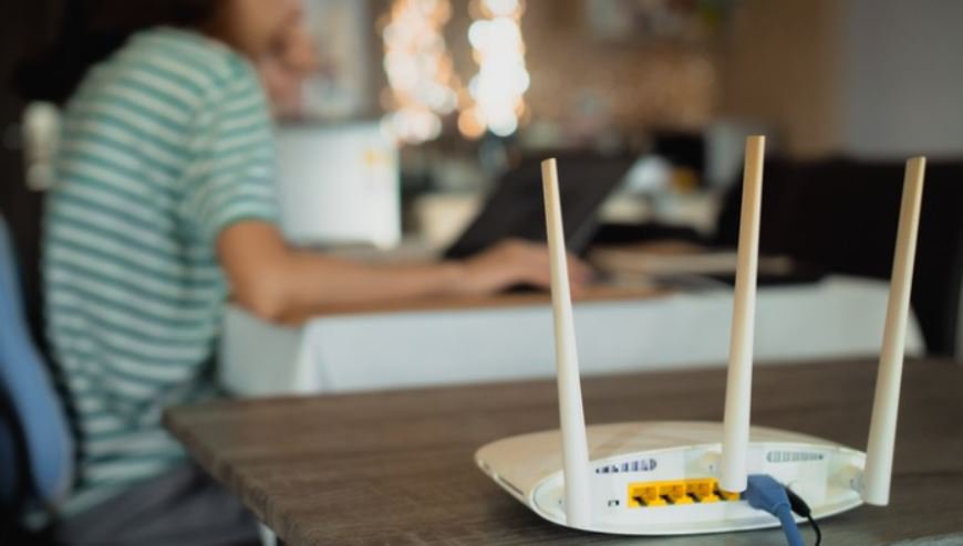 A wireless router with three antennas is prominently placed on a wooden table in the foreground.