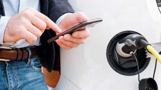 Photo of a man using his phone while charging an electric car