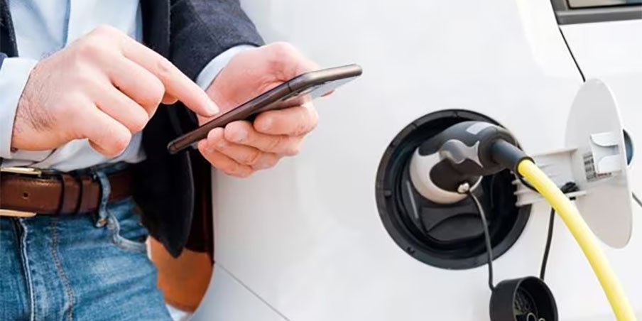Photo of a man using his phone while charging an electric car