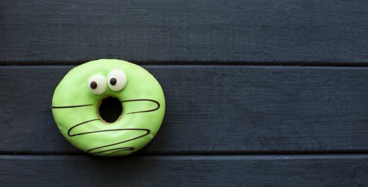 A vibrant green donut with a whimsical design featuring googly eyes and a surprised expression. 