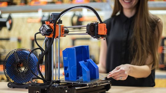 3D printer in operation, producing a blue plastic object.