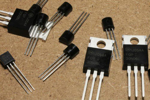 A collection of electronic transistors and power components is displayed on a textured brown surface.