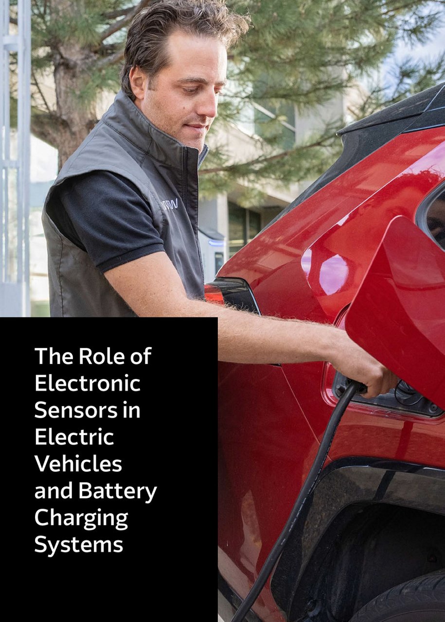 A person is seen plugging a charging cable into a red electric vehicle at an outdoor charging station. 