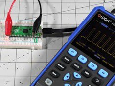 A blue handheld oscilloscope is shown capturing waveforms from a small electronic circuit on a white breadboard.