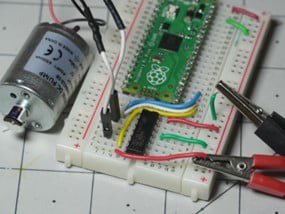 A Raspberry Pi Pico microcontroller is connected on a white breadboard alongside a small DC motor.