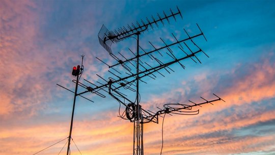 Un grupo de antenas de televisión al aire libre se muestra de manera prominente contra un cielo al atardecer vívido.