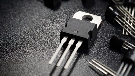 Un'inquadratura macro mostra un transistor elettronico a tre gambe posizionato su una superficie nera testurizzata.