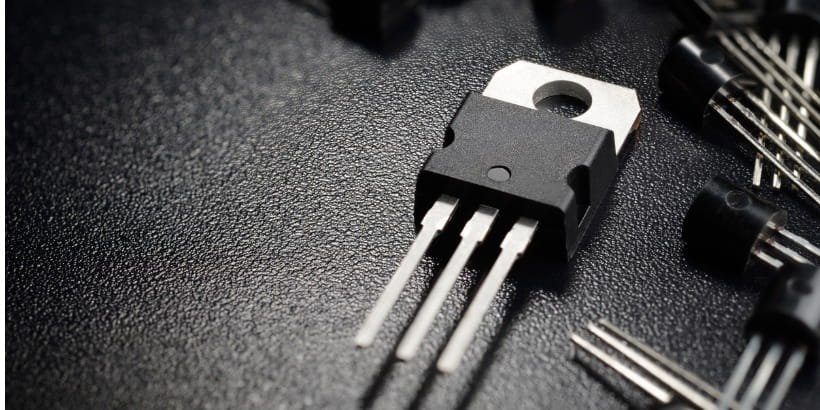Una toma macro presenta un transistor electrónico de tres patas colocado sobre una superficie negra texturizada.