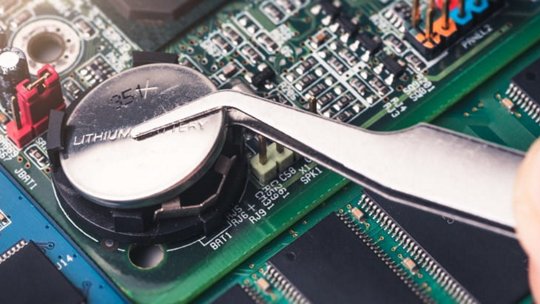 特写展示了一个锂电池正用金属镊子放置到计算机主板上。
