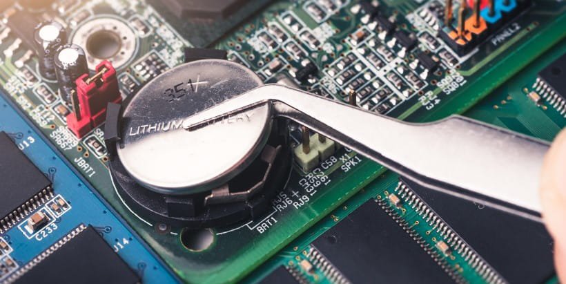 特写镜头显示用金属镊子将锂电池放置在计算机主板上。