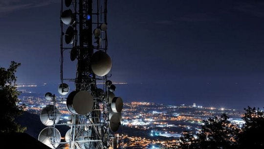 A large telecommunication tower with multiple satellite dishes and antennas stands prominently in the foreground.