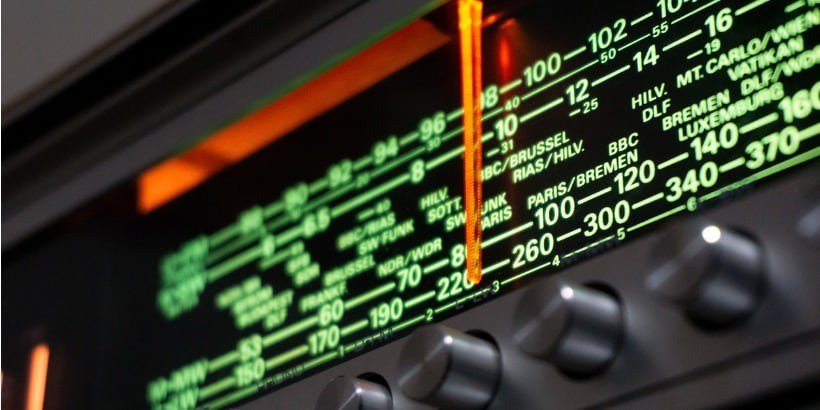 Una vista detallada de un sintonizador de radio vintage muestra marcas de frecuencia verdes iluminadas y un indicador de sintonización naranja brillante.