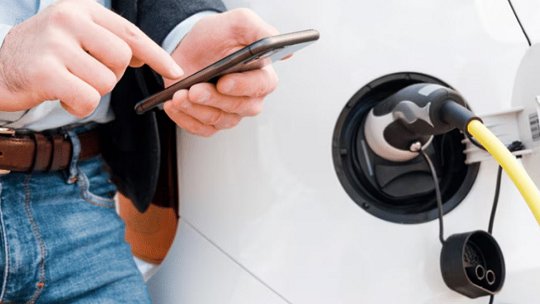 A man interacts with his smartphone while charging an electric vehicle. 