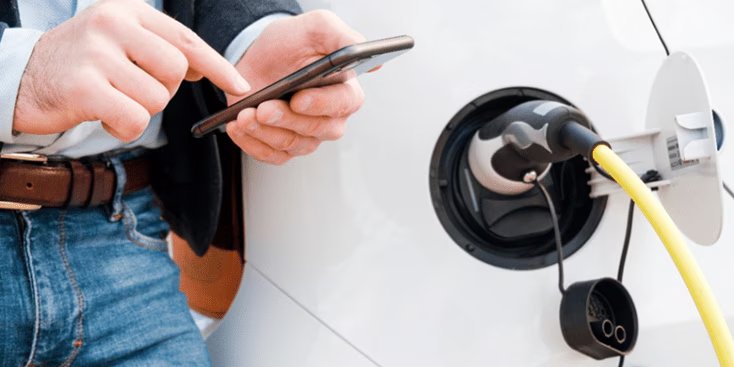 A man interacts with his smartphone while charging an electric vehicle. 
