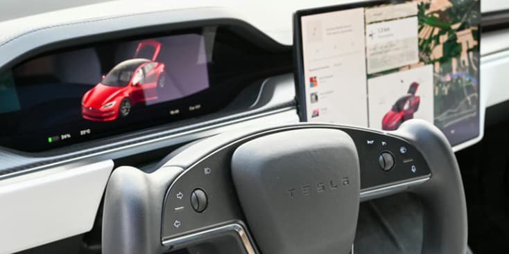 Vista ravvicinata dell'interno di un'auto Tesla che mostra un volante futuristico e doppi display digitali.