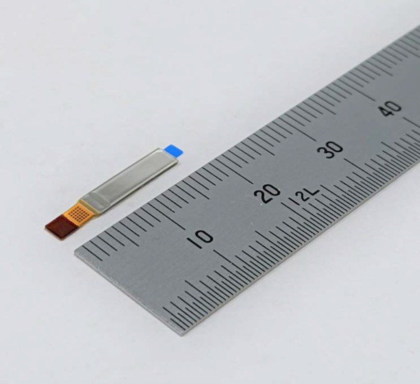 A close-up image of a small electronic component placed next to a metal ruler for scale.