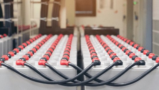 Un ampio assortimento di batterie industriali collegate con cavi neri e rossi è esposto in una struttura interna pulita.