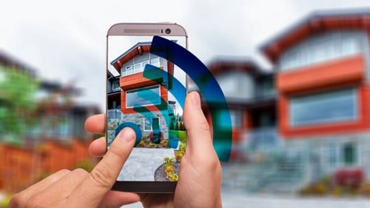 Un smartphone est tenu pour photographier une maison contemporaine avec des accents rouges et blancs.