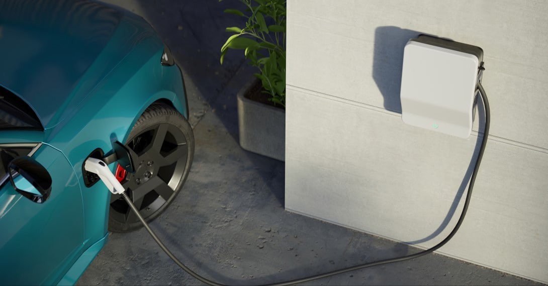 A sleek electric car is connected to a wall-mounted charging station in an outdoor setting.