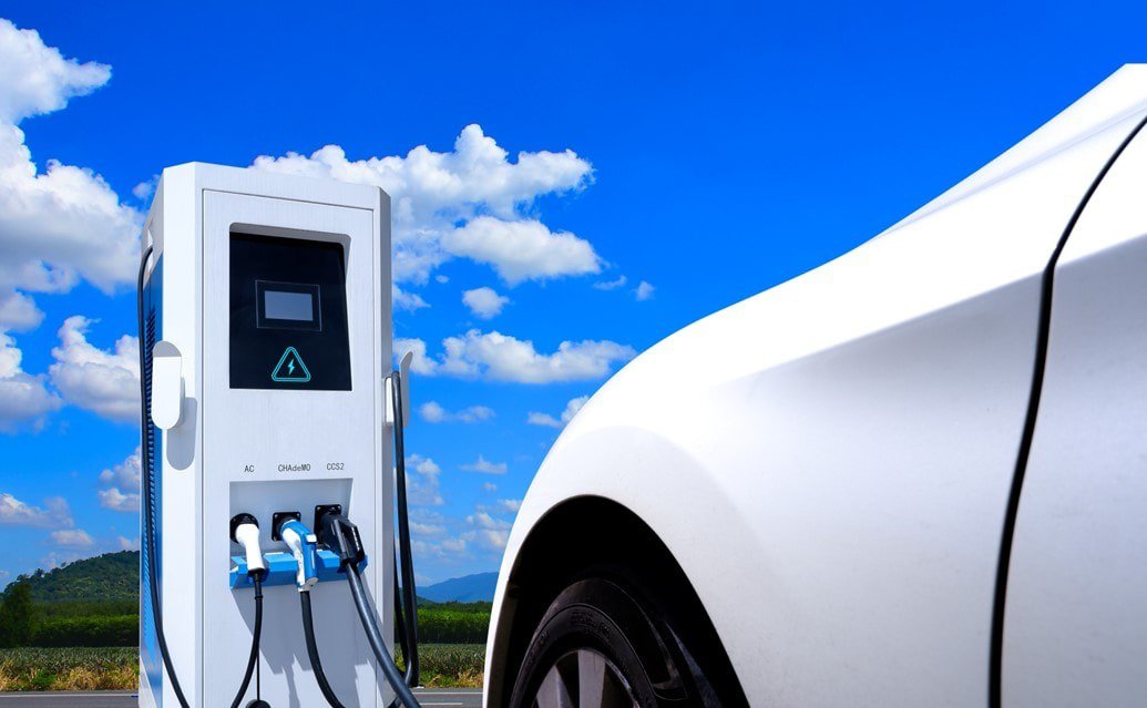 A modern electric vehicle charging station with multiple cables is shown in a sunny outdoor setting.