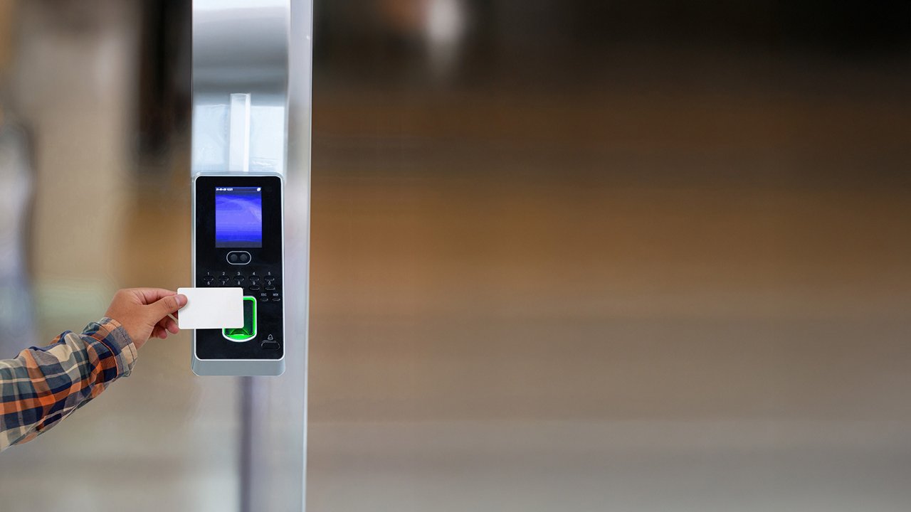 A person holds a white access card up to an electronic access control reader. 