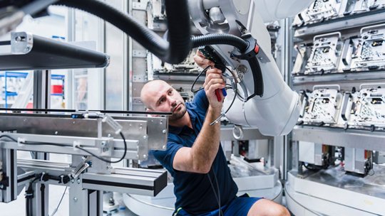 A technician works closely on a large industrial robotic arm inside a modern manufacturing facility.