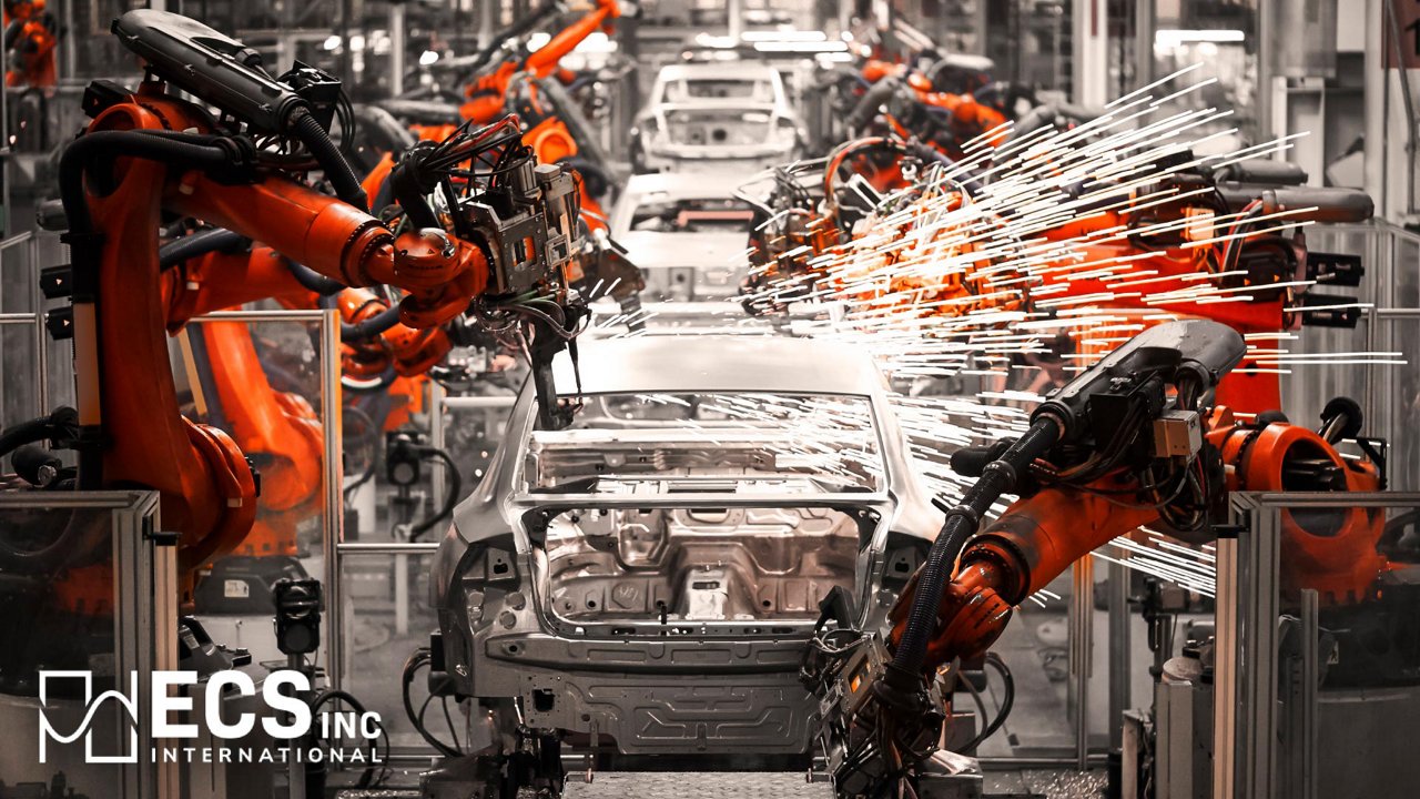 An unfinished car body is positioned on an automated assembly line surrounded by multiple robotic arms.