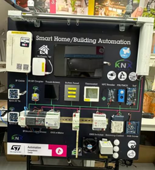 A demonstration board showcases a smart home and building automation system with various connected devices and modules. The setup includes a thermostat, button panel, NFC reader, dimming control, and RGB dimmer, all visibly labeled.