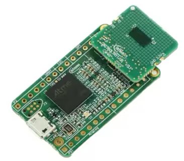 A compact green printed circuit board featuring an Atmel microcontroller is shown, with a secondary board attached on top. The main board includes a micro USB port and visible pin headers along the sides.