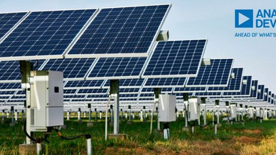File di pannelli solari montati a terra in un grande impianto fotovoltaico, con strutture di supporto metalliche e scatole di controllo elettrico sotto i pannelli, che si estendono in lontananza su un campo erboso sotto un cielo sereno. Il logo Analog Devices appare nell'angolo in alto a destra.