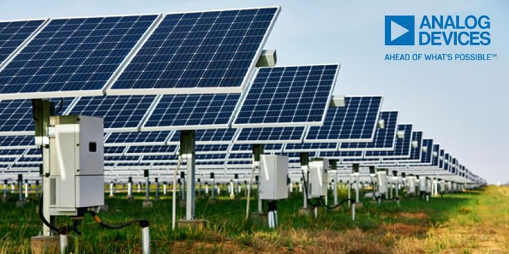 Rows of ground-mounted solar panels in a large photovoltaic farm, with metal support structures and electrical control boxes beneath the panels, extending into the distance across a grassy field under a clear sky. The Analog Devices logo appears in the upper right corner.