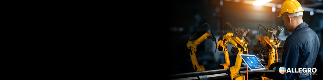 Un ingeniero de fábrica con un casco amarillo opera una tableta junto a varios brazos robóticos amarillos. 