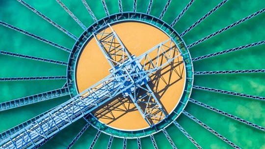 A striking aerial view of a circular industrial water treatment facility with a vibrant green and orange color palette.