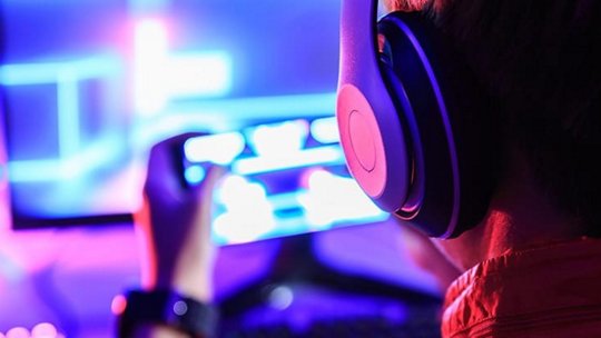 Une personne portant des écouteurs circum-auraux est immergée dans le jeu, tenant une manette dans un environnement vibrant éclairé au néon.