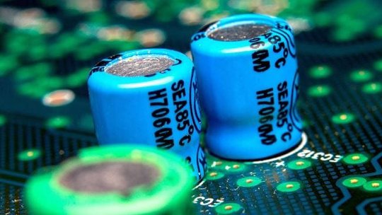 蓝色电容器上标有 SEA85°C H706CM，安装在绿色电路板上的详细视图。