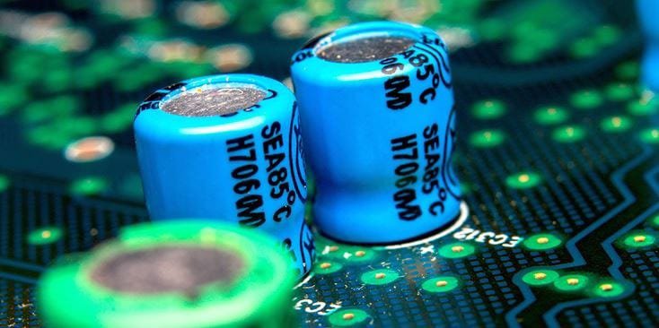 蓝色电容器的详细视图，标有SEA85°C H706CM，安装在绿色电路板上。