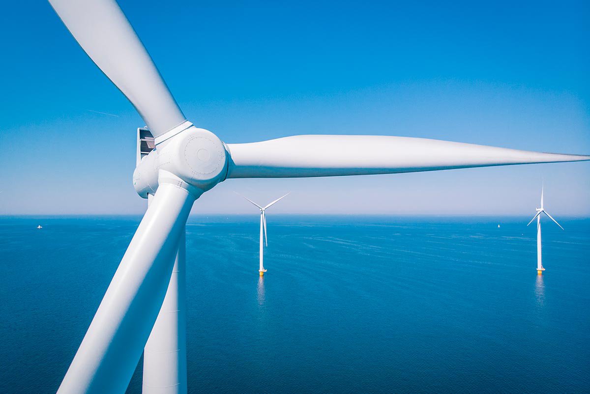 Large white wind turbines stand in the ocean, generating renewable energy. 
