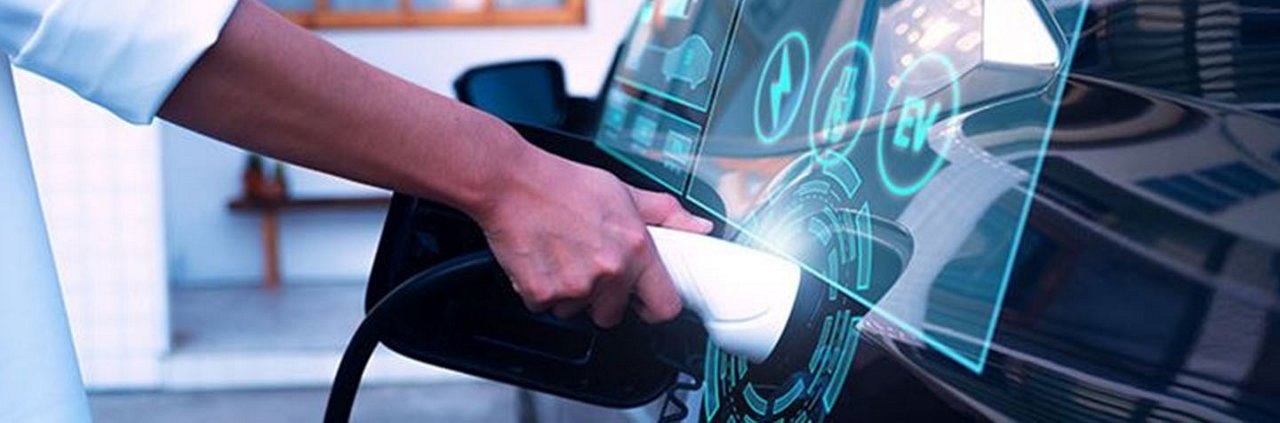 A close-up of a person plugging a charging cable into an electric vehicle at a modern charging station. 