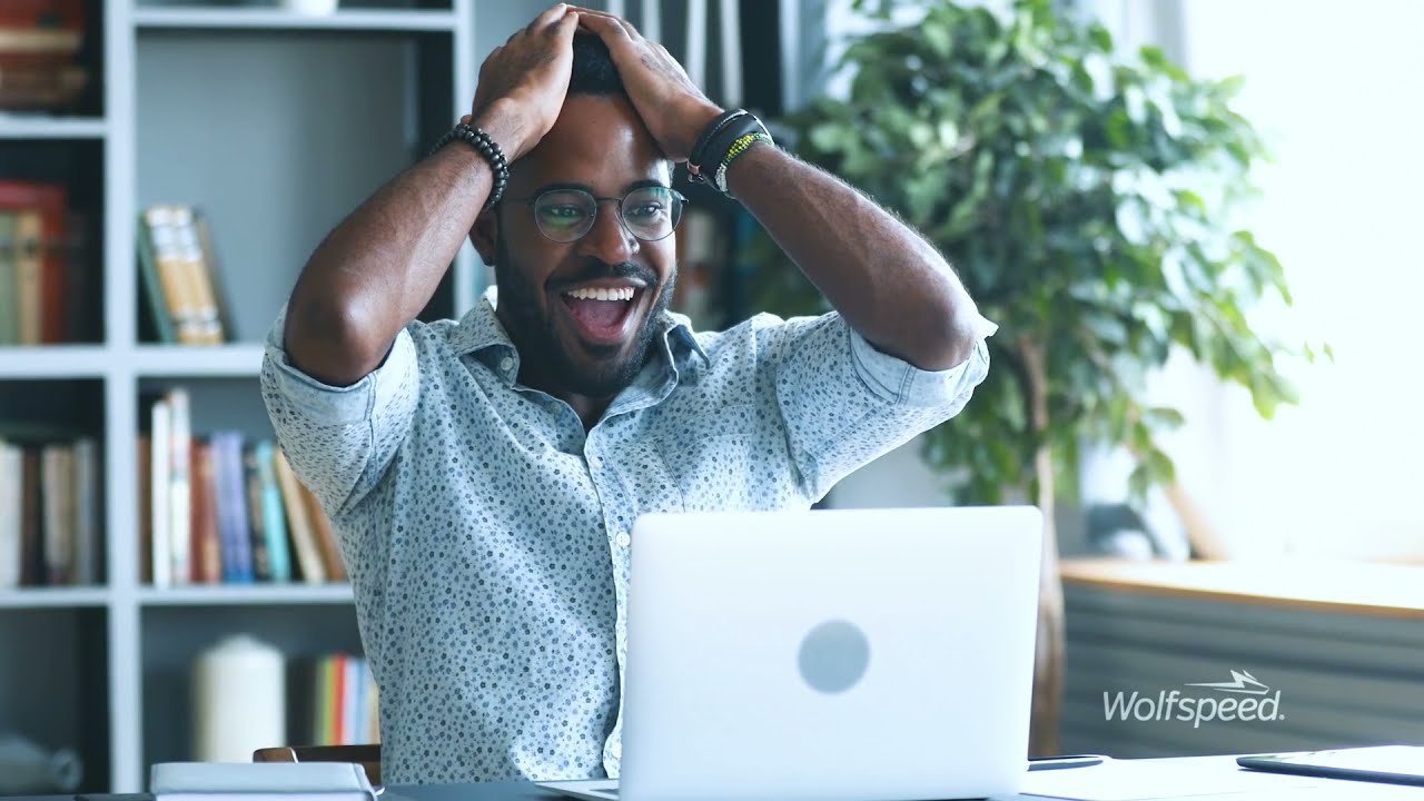A man sits at a desk with his hands on his head, appearing frustrated. 