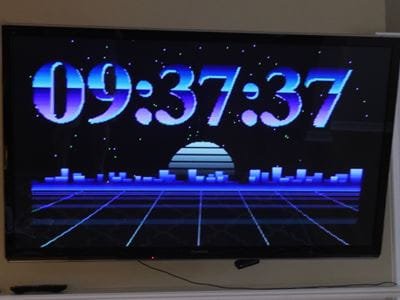 Television screen displaying a digital clock with large blue numerals showing the current time against a stylized grid background.