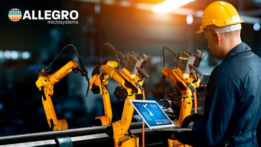 An industrial engineer wearing a yellow hard hat monitors multiple yellow robotic arms on an automated production line. 