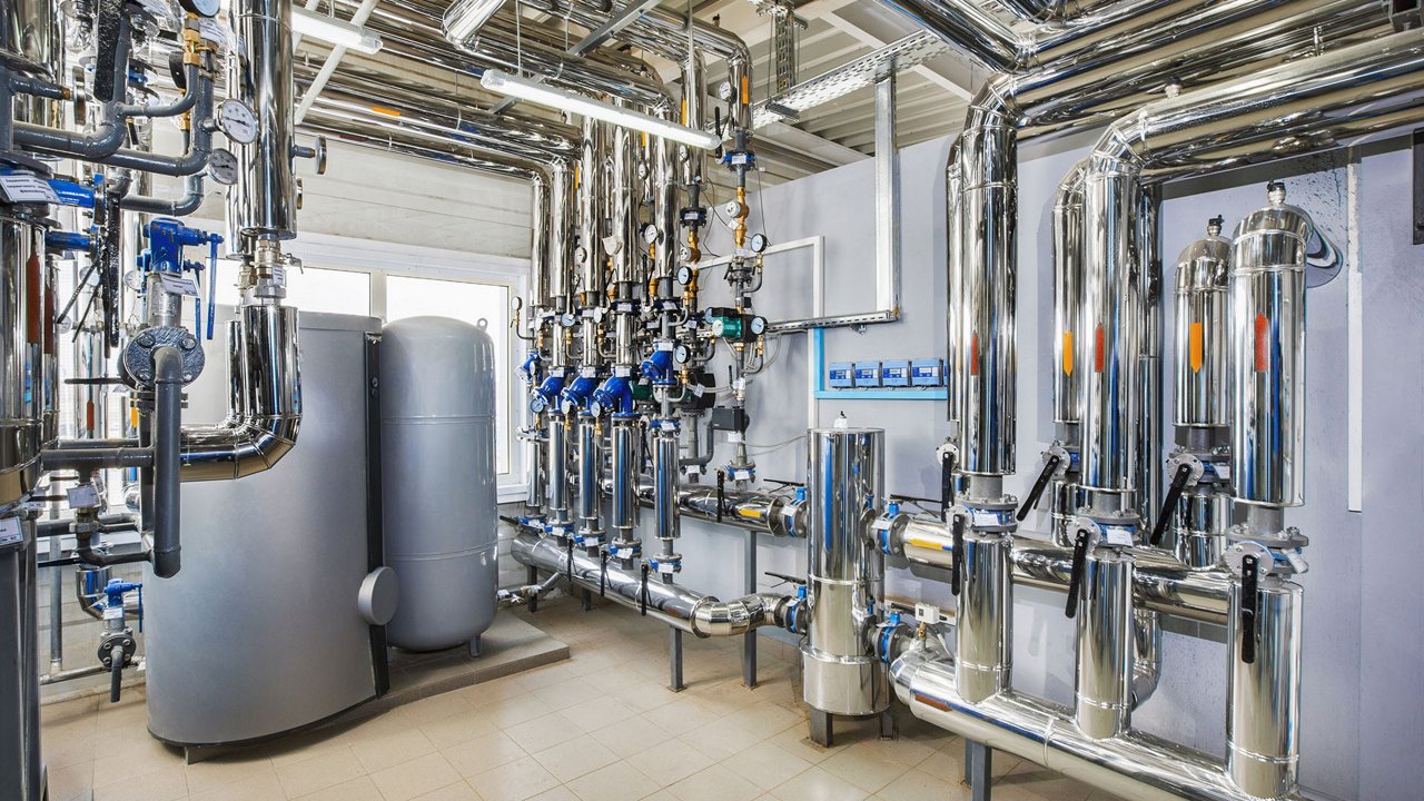 A modern industrial boiler room featuring an array of polished metal pipes, tanks, and valves. 