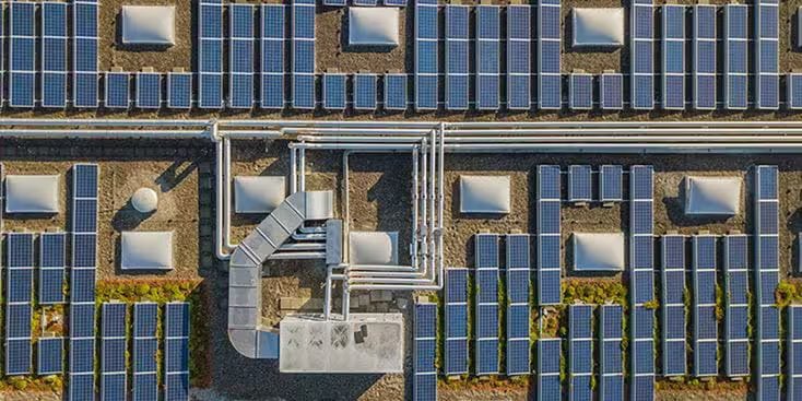 Une série de panneaux solaires installés sur un toit plat, vue d'en haut. Des conduits industriels et des systèmes de ventilation proéminents traversent le centre, entourés de modules solaires espacés uniformément.
