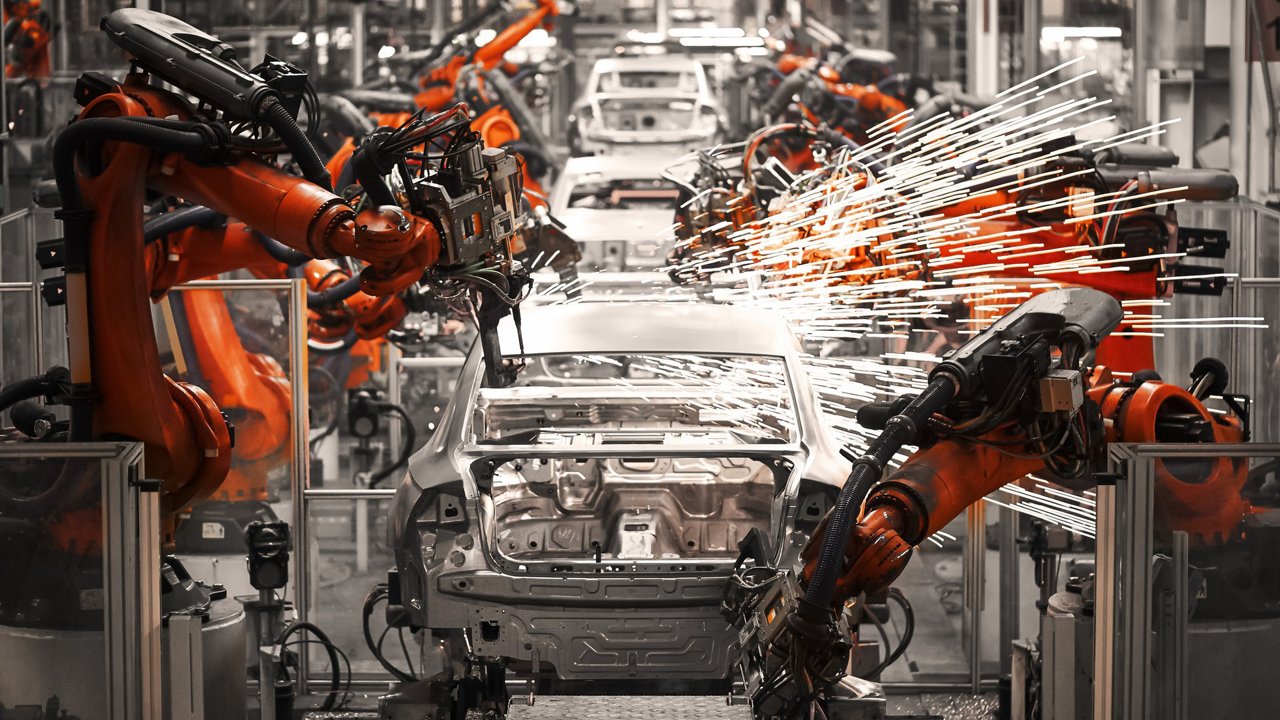 Industrial robotic arms work on assembling a car frame in a modern manufacturing facility