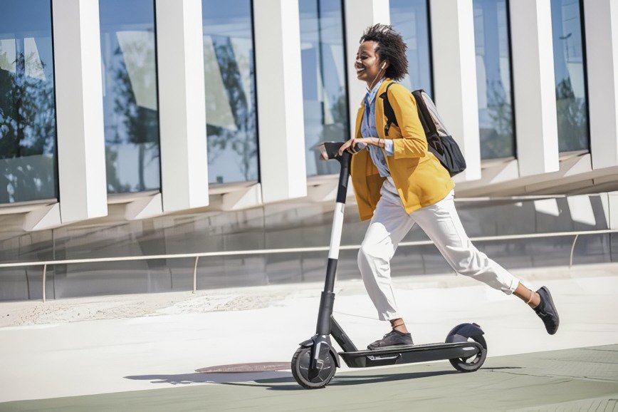 A person in a yellow jacket rides an electric scooter on a sunny day.