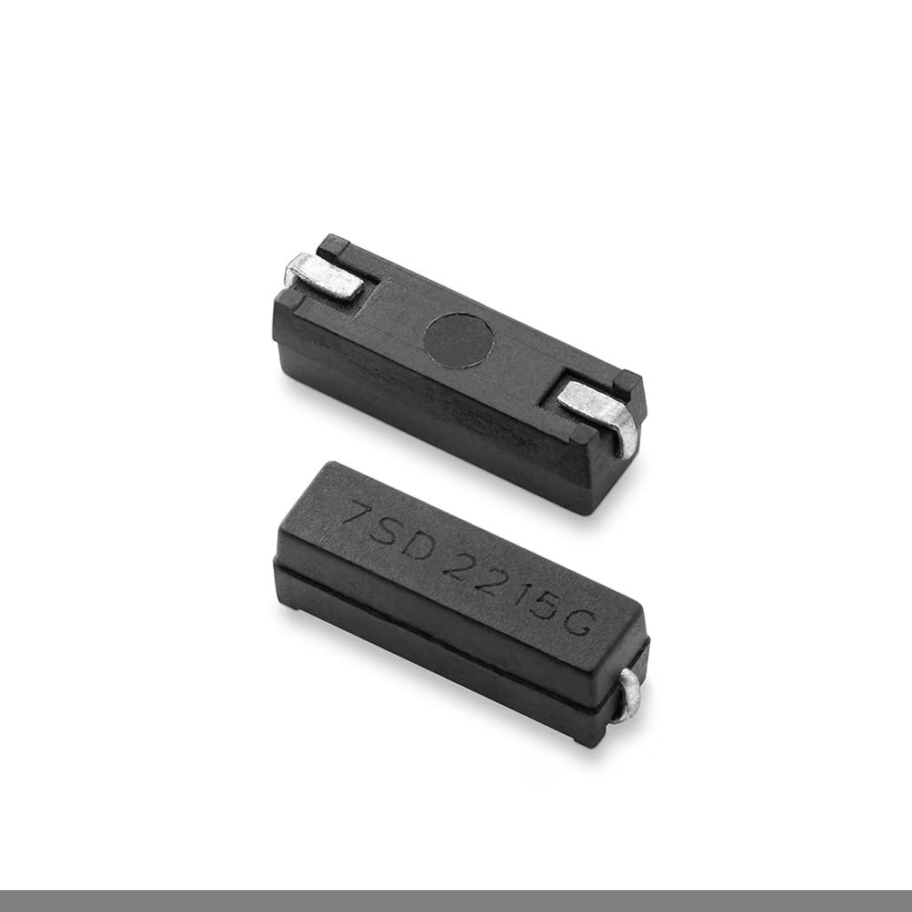 Close-up of two small black rectangular reed switch components placed on a white background. One component is positioned flat, displaying the marking '7SD 2215G' clearly on its surface. The other component is angled to show its metallic contacts.