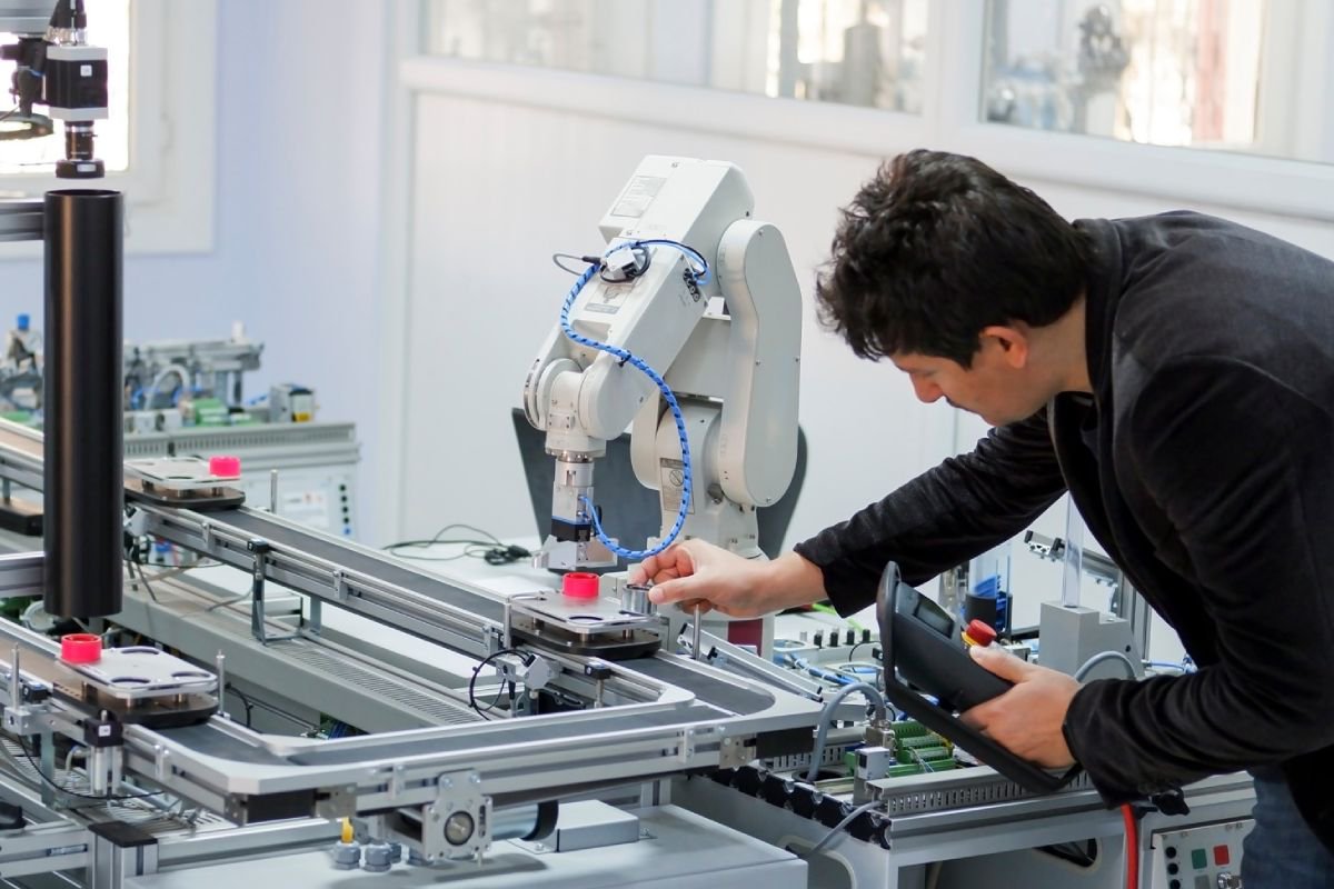 A male engineer operates and calibrates a robotic arm within a modern industrial laboratory. 