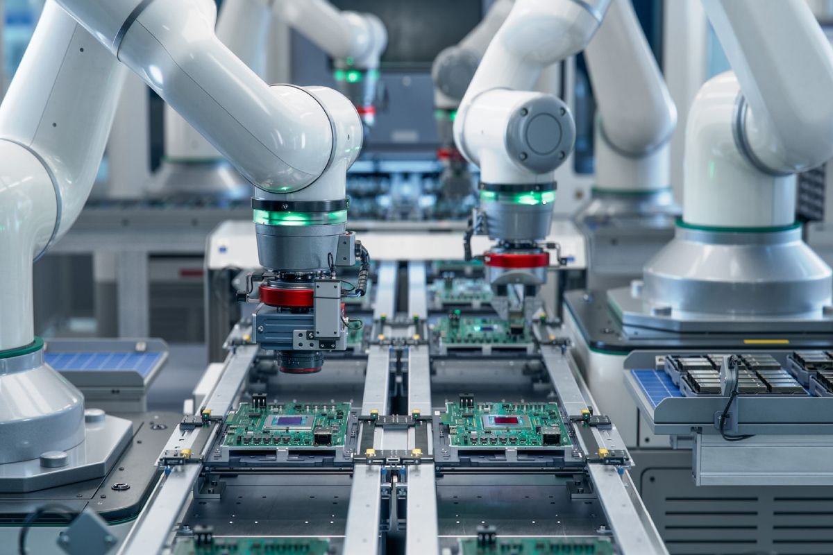 Multiple robotic arms are seen precisely assembling green circuit boards on a conveyor system in a modern industrial facility. 